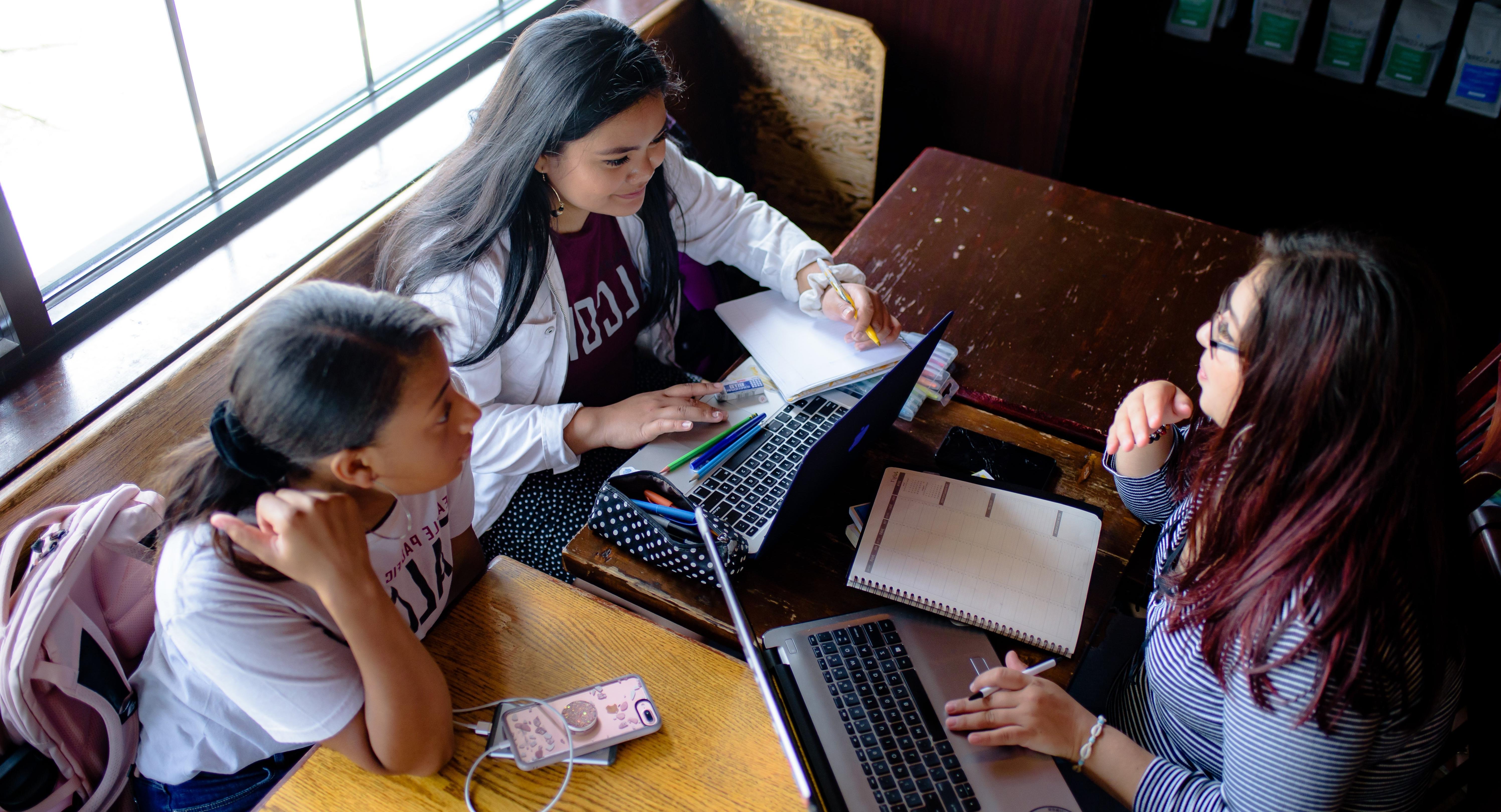 Three students study together at a cafe table