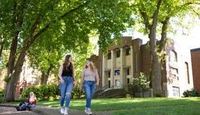 Two SPU students walk and talk in Tiffany Loop, with McKinley Hall in the background.